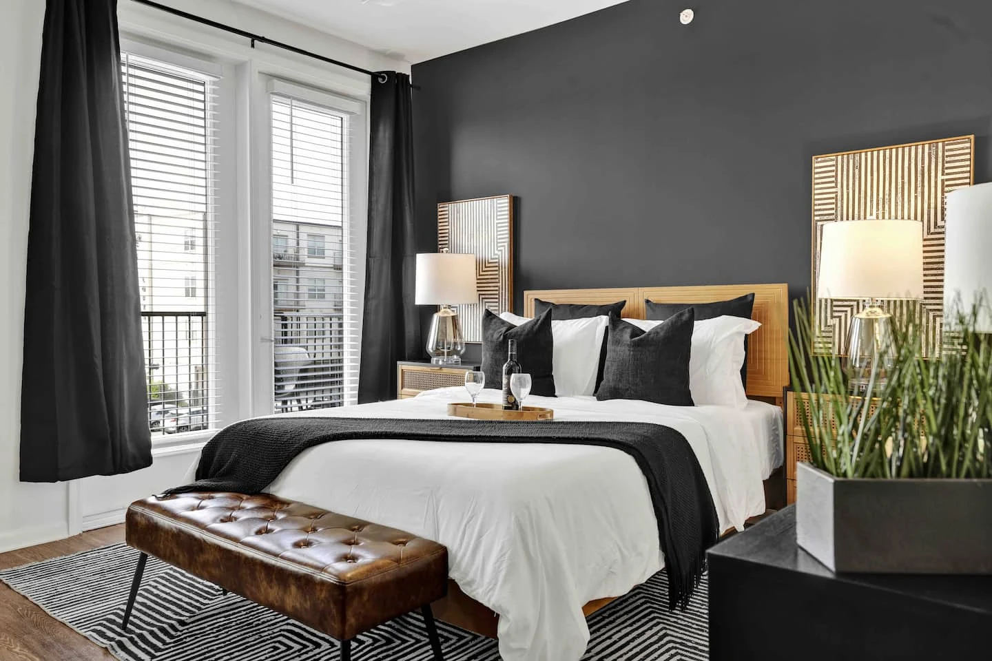 Boho Black bedroom with white linens, dark cushions, warm wood furniture and tall windows