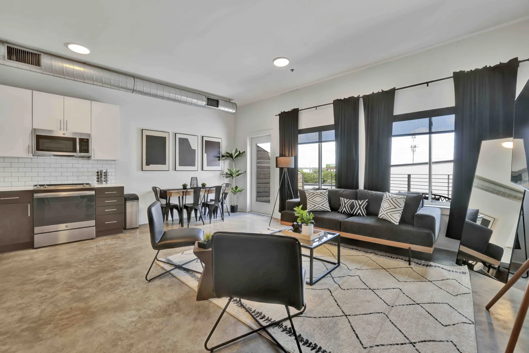 Light-filled loft with an open kitchen, dark sofa, dining area, and large windows